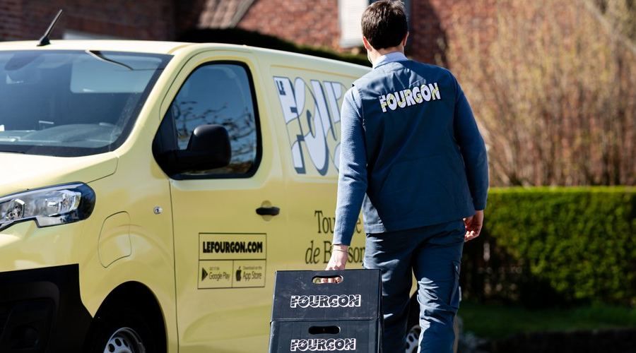 Un livreur Le Fourgon porte une caisse de bouteilles consignées