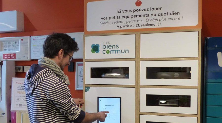 Une personne loue un objet aux casiers Les Biens en Commun, chez un commerçant