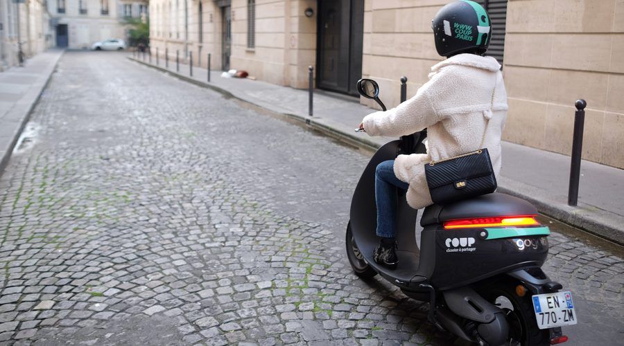Une utilisatrice sur un scooter électrique Coup dans une rue pavée de Paris